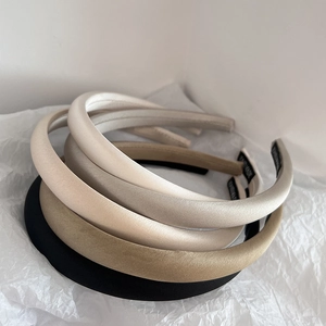 Stack of thin satin headbands in beige and black colors on white paper background
