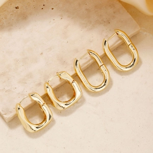 Detail of gold rectangular thick hoop earrings displayed on a beige textured stone surface