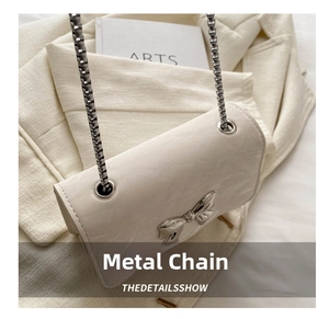 Detail of cream leather mini bag featuring silver metal bow clasp and chain strap