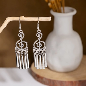Detail of vintage silver treble clef earrings with metallic tassels on a wooden branch