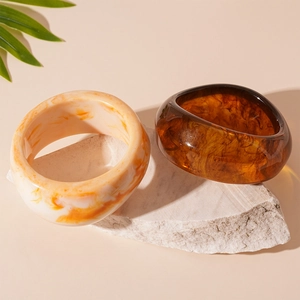 Detail of amber and cream resin bangles stacked on white stone with green leaves
