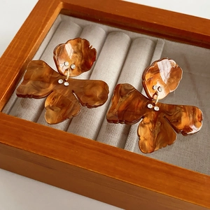 Detail of flower-shaped brown marble resin earrings with small diamond accents in a box