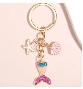 Detailed macro shot of mermaid tail, starfish, and pearl shell charms on a gold keychain