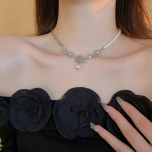 Close-up of asymmetric pearl and silver chain necklace with a green gemstone flower