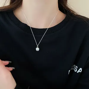 Close-up of minimalist silver apple pendant necklace worn by a model on black sweater
