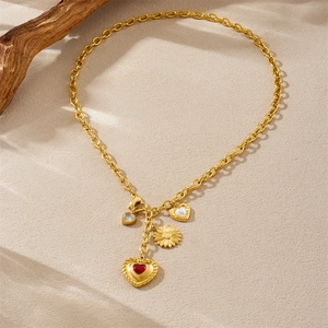Gold-plated necklace with red heart, pearl, and sunflower charms on a textured surface