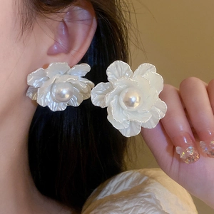 Close-up of white flower pearl earring on ear and hand, elegant silver needle jewelry