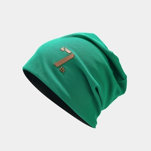 Close-up of green ribbed knit beanie featuring a brown leather patch with 7th engraving