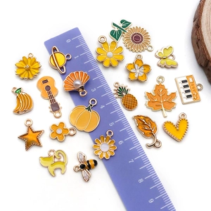 Assorted yellow enamel alloy floral and fruit charms shown with ruler for size reference