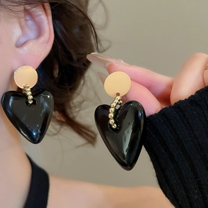 Close-up of black heart earrings with gold base and chain on model for size reference