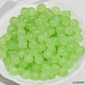 Macro view of green 6x8mm barrel-shaped craft beads in a white floral dish