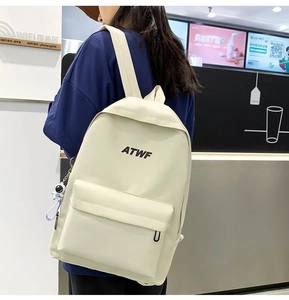 Detailed view of cream-white backpack with ATWF print and astronaut keychain on shoulder