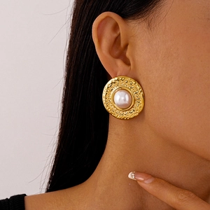 Close-up of vintage golden hammered metal earrings with large white pearl on model