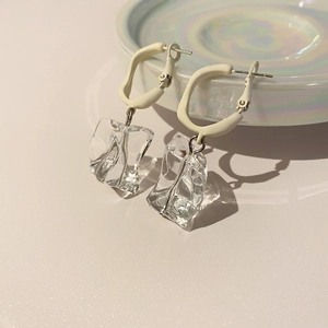 Close-up of irregular clear acrylic ice-shaped pendants with beige matte hoop earrings