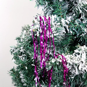 Shiny purple Christmas tinsel garland hanging on a snow-covered green pine tree branch
