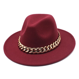 Detail of burgundy wool fedora hat featuring a chunky gold chain accessory on white background