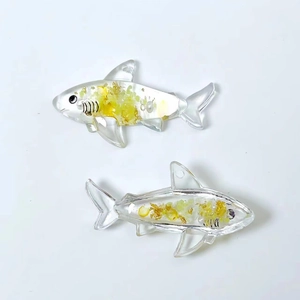 Macro detail of shark shaped resin pendant with gold foil leaf on white background