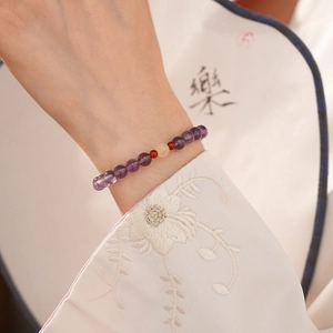 Detail of beaded bracelet with amethyst and agate worn against a traditional fan background