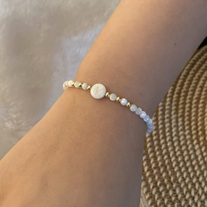 Detail of beaded shell bracelet with golden letter V charm on a textured background