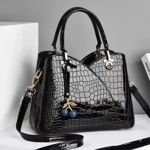 Detail of black crocodile texture bag with glossy finish and cherry bag charm accessory