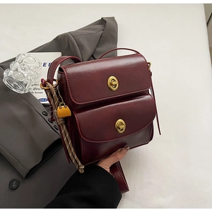 Detail of burgundy leather crossbody bag with double gold twist locks and woven knot charm