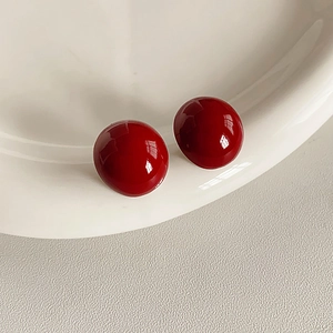 Detail von roten kugeligen Ohrsteckern mit glänzendem Finish auf weißer Keramik
