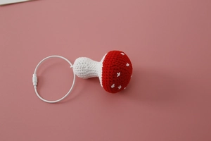 Macro detail of a hand-knitted red mushroom keychain with white spots and cotton texture