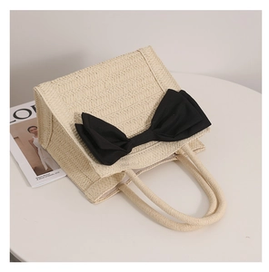 Close-up of beige woven straw tote bag featuring a large black fabric bow and texture
