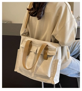 Close-up of a cream canvas tote bag with brown straps and large front pockets