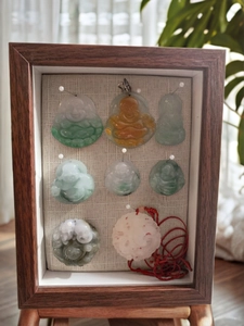 Detail view of jade Buddha pendants displayed in a dark wooden frame with linen backing