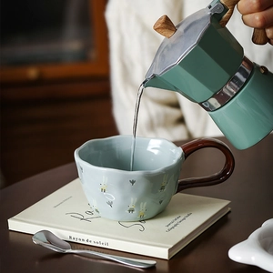 Ceramic bunny mug in light blue-green with a brown handle and metal spoon on a wood desk