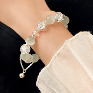 Detailed view of beaded bracelet with light green translucent beads and a silver bell charm