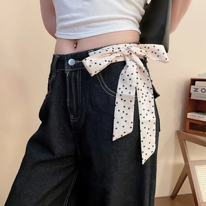 Dettaglio di jeans blu con un foulard di seta a pois neri usato come cintura alla moda