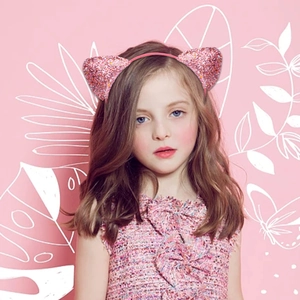 Pink sequin cat ear headband worn by a young girl on a playful illustrated background