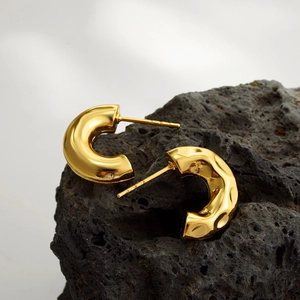 Macro shot of gold C-shaped earrings with hammered and polished textures on black lava stone