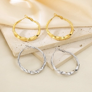 Detailed view of gold and silver twisted C-shaped earrings on elegant silk background