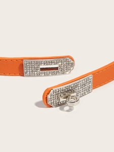 Close-up of adjustable orange leather waist belt with rhinestone buckle and textured finish