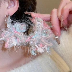 Detail showing oversized yarn flower earrings with pearls and soft pastel textures
