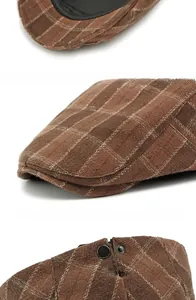 Detail view of brown plaid flat cap showing rigid brim and metal adjustable buckle