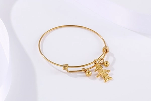 Détail d'un bracelet ouvert doré avec pendentif garçon et perles sur fond de soie blanche