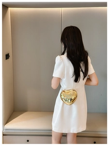 Rear view of model wearing a metallic gold heart-shaped acrylic crossbody bag with chain