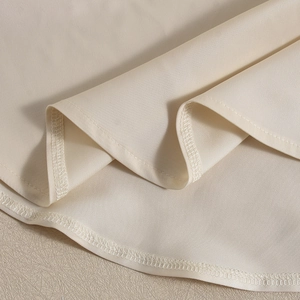 Close-up of fine stitching on the cream satin asymmetrical hemline of this sleeveless top