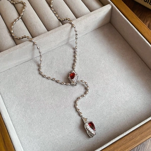 Macro detail of silver Y-shaped necklace with red teardrop stones on velvet tray