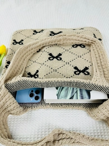 Top-down macro view of beige knitted tote bag showing black bow pattern and knit texture