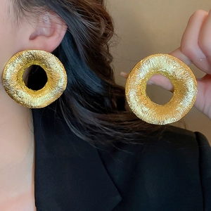 Detail of large gold hoop earrings featuring a unique molten lava texture and metallic finish
