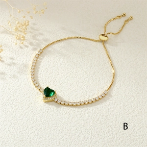 Macro detail of gold adjustable heart bracelet featuring a green gem and pave crystals