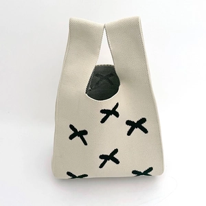 Detail of beige knitted tote bag with black cross pattern and textured fabric handles
