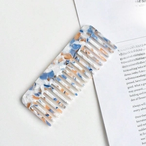 Macro shot of blue and orange marble-patterned cellulose acetate wide-tooth comb on book
