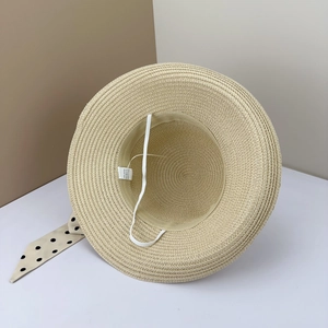 Detailed interior of a beige paper straw hat with white chin strap and care label