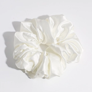 Detailed view of a white satin scrunchie showing glossy silk texture and rich folds
